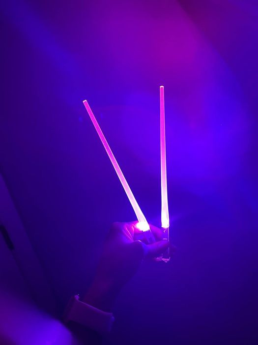 A hand holding two glowing light sticks in a dark environment, perfect for concerts or parties