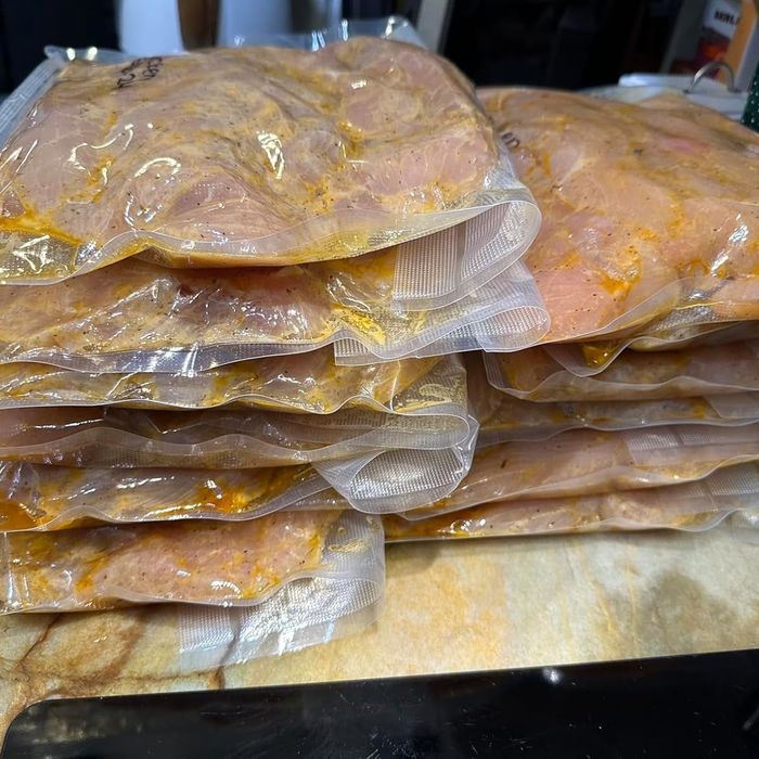 Vacuum-sealed bags, stacked on a counter, each contain marinated raw chicken breast fillets.
