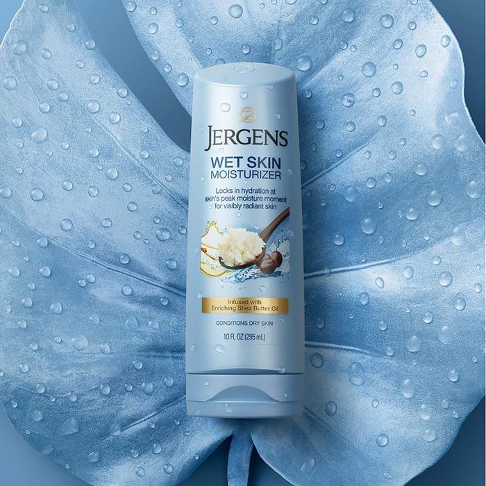 The bottle of lotion resting on a wet, blue leaf