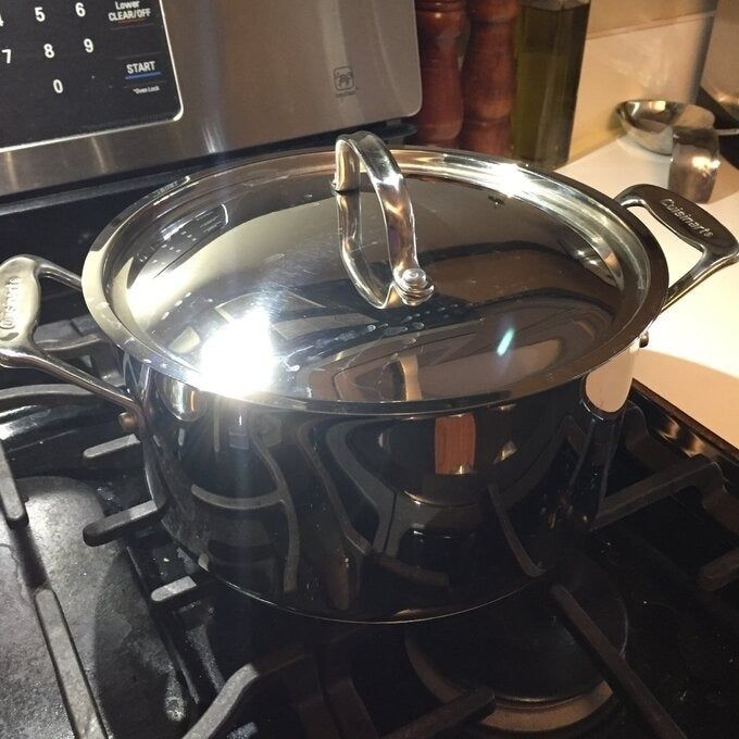 A gleaming stainless steel pot with a matching lid resting on a stove in a cozy kitchen setting.