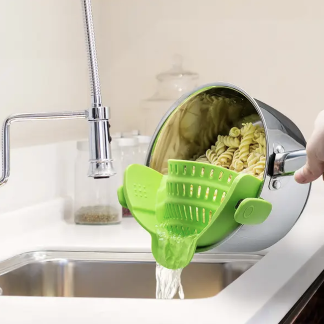 A model straining pasta from a green strainer clipped to the sides of a pot