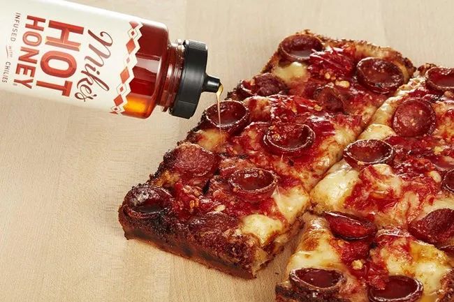 drizzling Mike's Hot Honey onto a pepperoni pizza