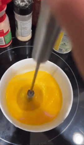 A reviewer pressing down on the rotating whisk to beat eggs.