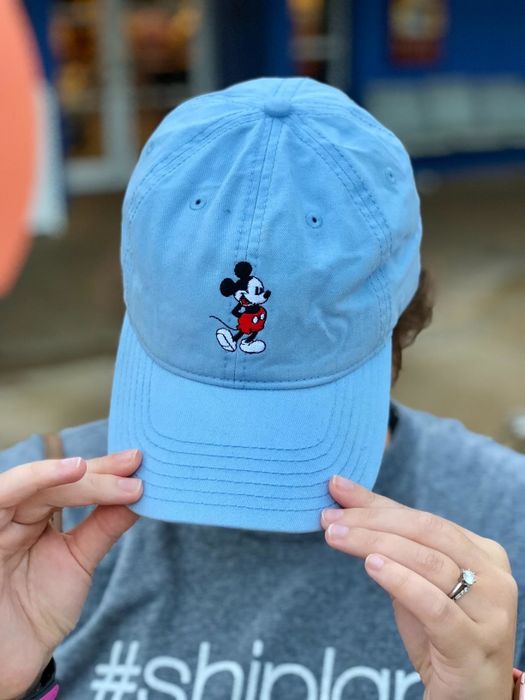A reviewer tipping down a light blue cap with Mickey embroidered on the front