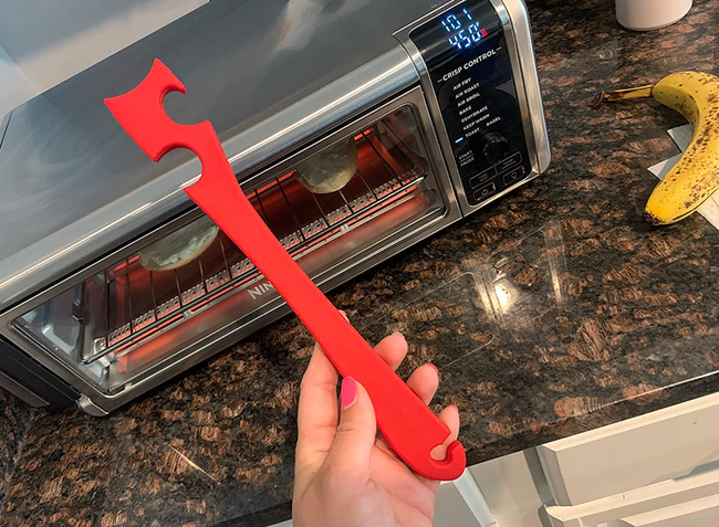 A reviewer holding a red, hooked tool beside a toaster oven