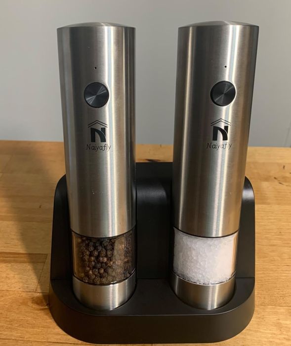 Stainless steel electric salt and pepper grinders by Najiafly, placed on a wooden countertop.