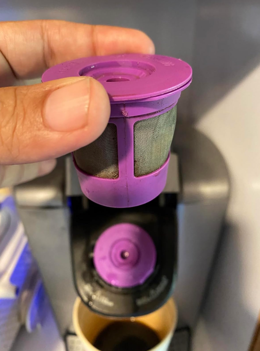 A person holding a reusable coffee filter pod above a coffee machine