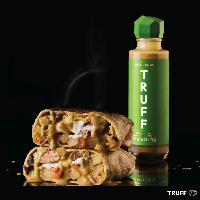 A burrito stuffed with meat, cheese, and veggies, accompanied by a bottle of Truff Hot Sauce on the side