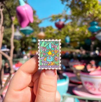 A model holding a stamp-shaped pin featuring an Alice in Wonderland design