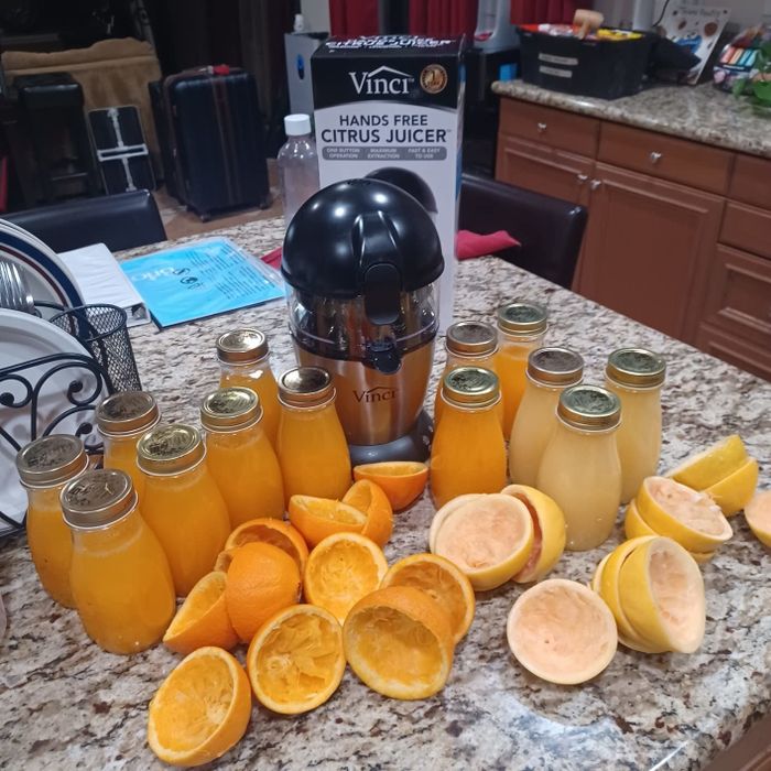 Hands-free citrus juicer surrounded by jars of fresh juice and discarded orange peels on a kitchen counter