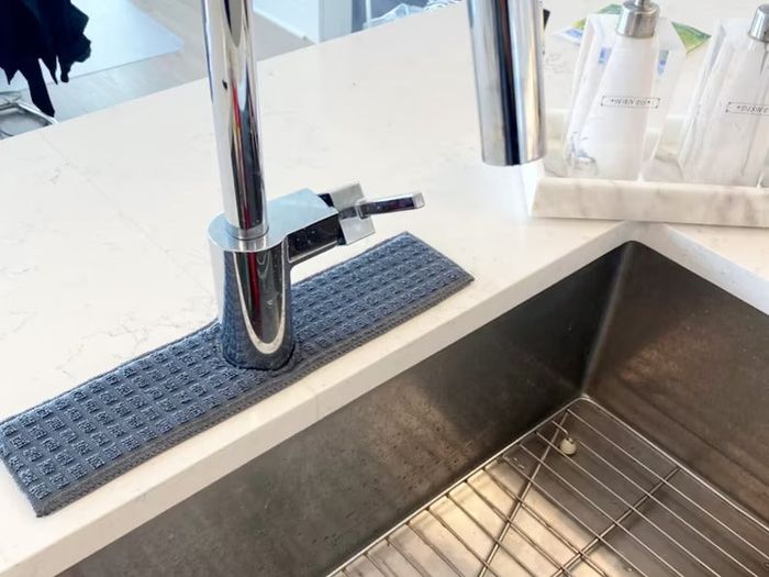 A gray rectangular sink bib positioned around the faucet