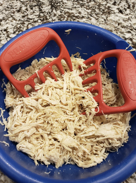 The shredder claws placed on top of a bowl filled with shredded chicken.