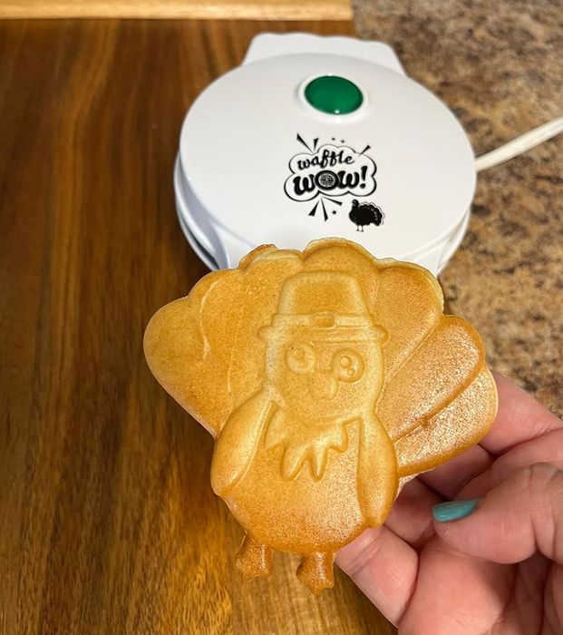 A turkey-shaped waffle being held in hand, with a waffle maker in the background