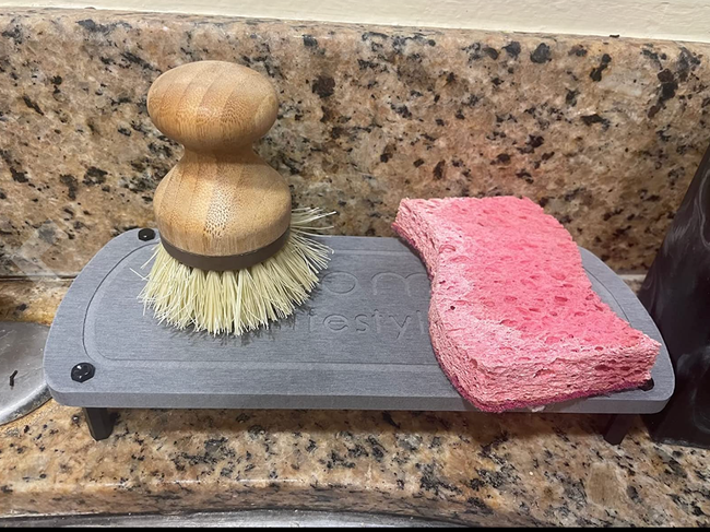A sleek, rectangular gray caddy holding a soap brush and sponge, ready for use