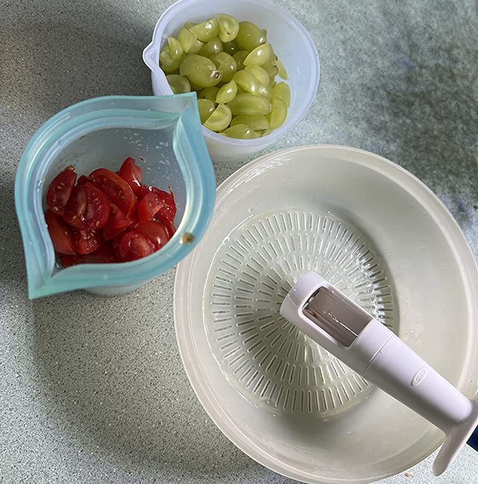 A photo of the reviewer showing containers filled with quartered grapes and cherry tomatoes, placed next to the grape cutter.