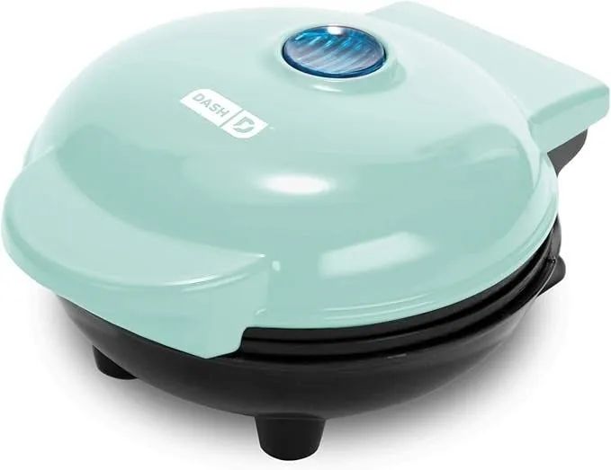 A compact, round Dash mini waffle maker featuring a handle and an indicator light on top