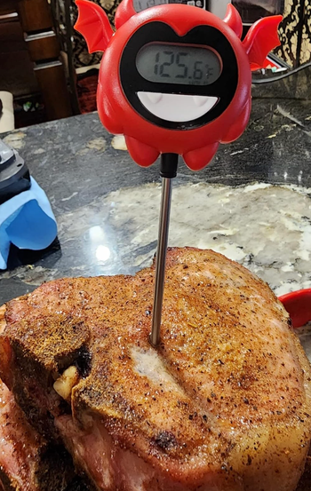 A thermometer embedded in a piece of meat with a digital display featuring a cute red demon design