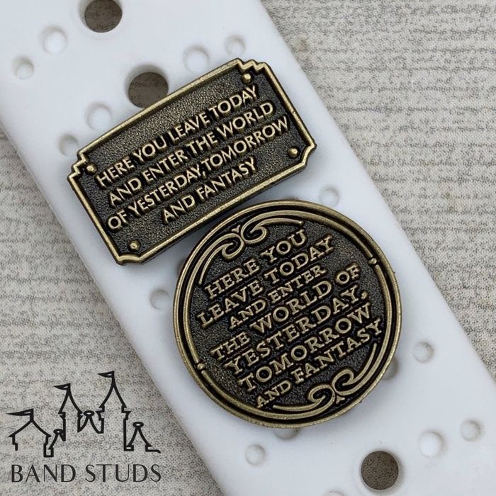 Two charms on a watch band resembling plaques from Disney World and Disneyland