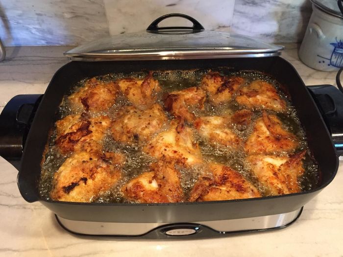 Pieces of chicken frying in an electric skillet on a kitchen counter