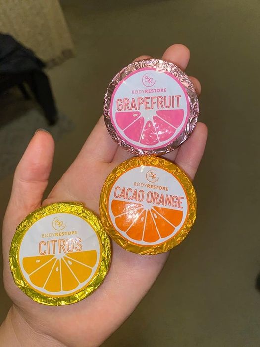 A customer's photo showing a hand holding three wrapped shower steamers in Cacao Orange, Grapefruit, and Citrus scents