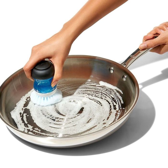 someone scrubbing a soapy pan with a palm-sized soap-filled dish brush