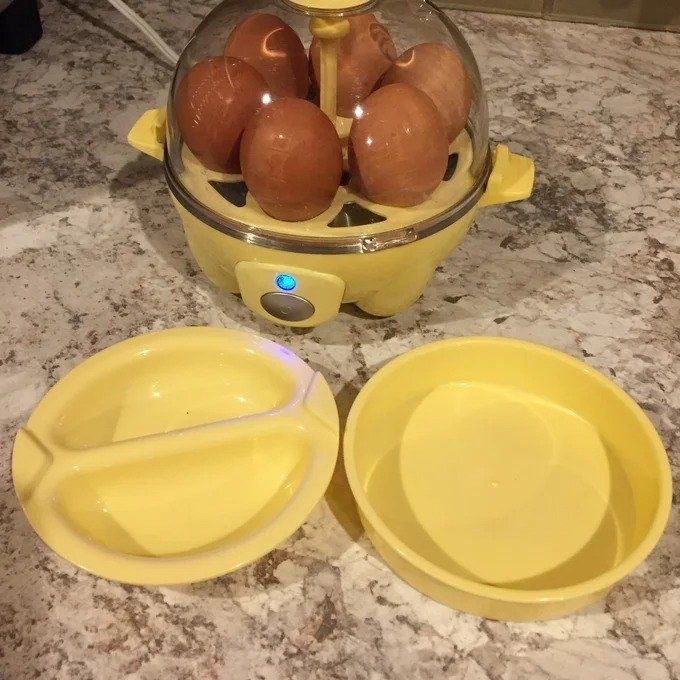 An egg cooker with several eggs inside, placed on a kitchen countertop next to two yellow divided plates