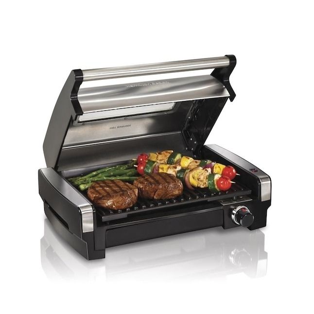 An indoor grill with the lid open, displaying steaks, vegetables, and skewers