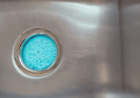 Blue foaming cleanser emerging from the sink drain
