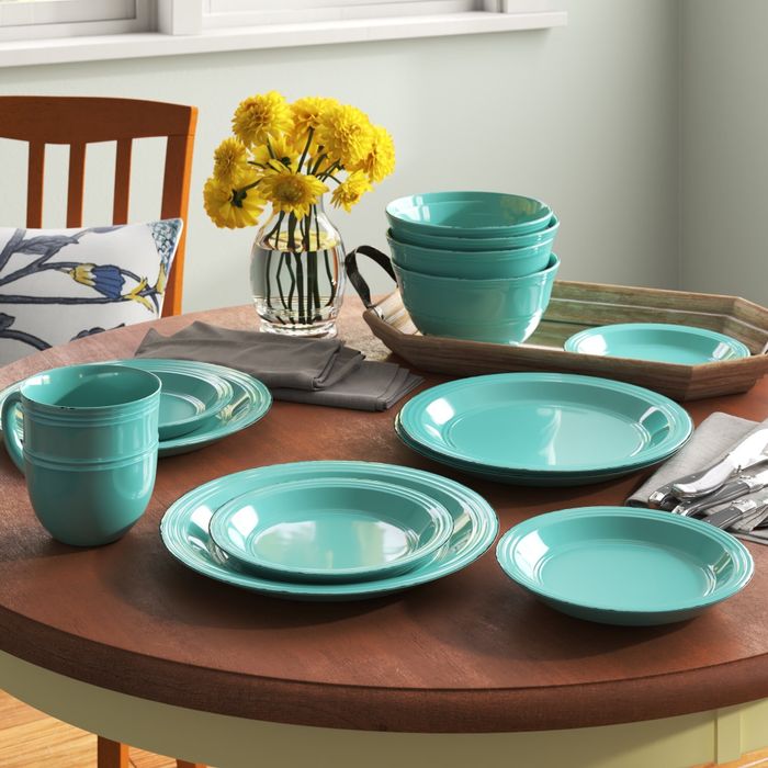 A collection of turquoise dishware items, including plates, bowls, and mugs, set beautifully on a round table with a vase of yellow flowers, highlighting a home dining set