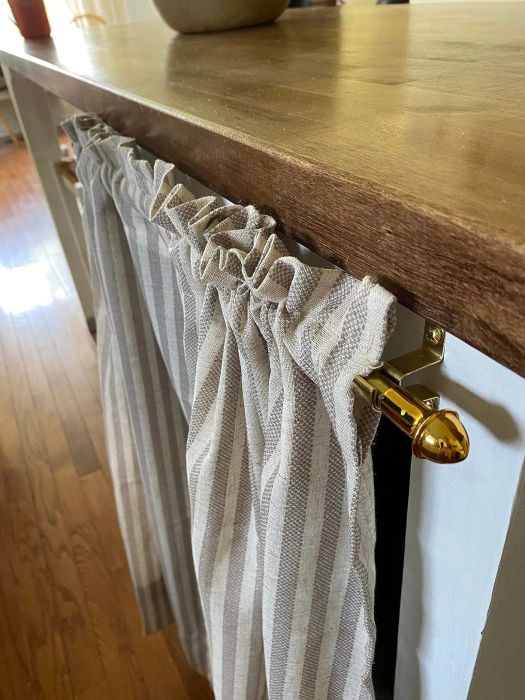 A close-up view of a farmhouse-inspired curtain with a striped design, draped on a brass rod beneath a rustic wooden table.