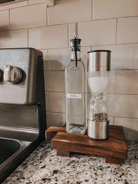 A kitchen counter showcasing an olive oil bottle and a salt and pepper grinder, placed on a wooden tray next to a stove