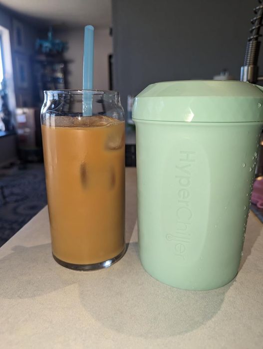 a glass of iced coffee alongside a mint-colored HyperChiller on a table