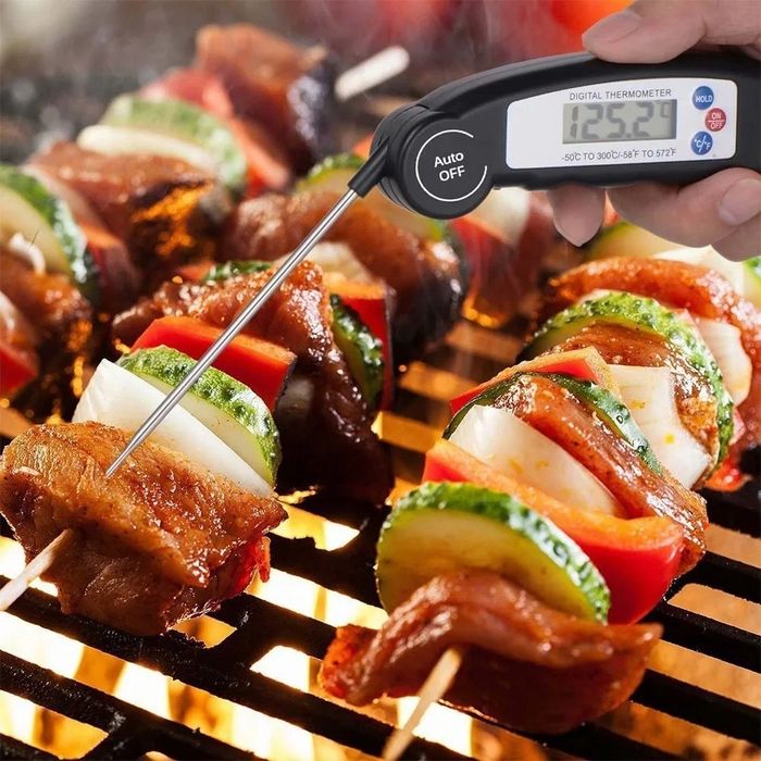 The meat thermometer with a large probe measuring the temperature of a meat skewer.