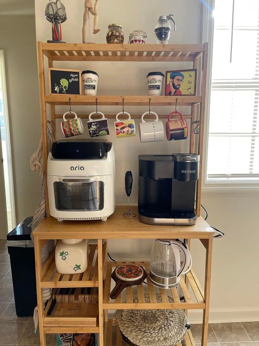 A wooden kitchen shelf holding an air fryer, Keurig coffee maker, kettle, mugs, spices, and some decorative pieces