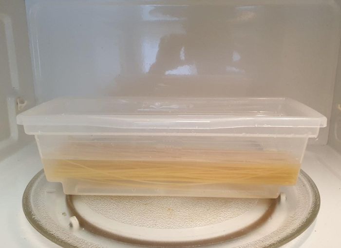 A pasta cooker filled with pasta and water, placed inside the microwave, ready to cook