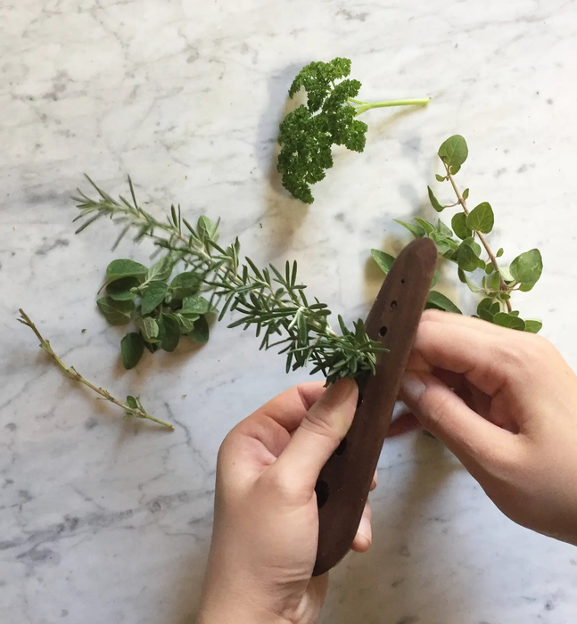 Hands feeding a sprig of rosemary through a wooden herb stripper