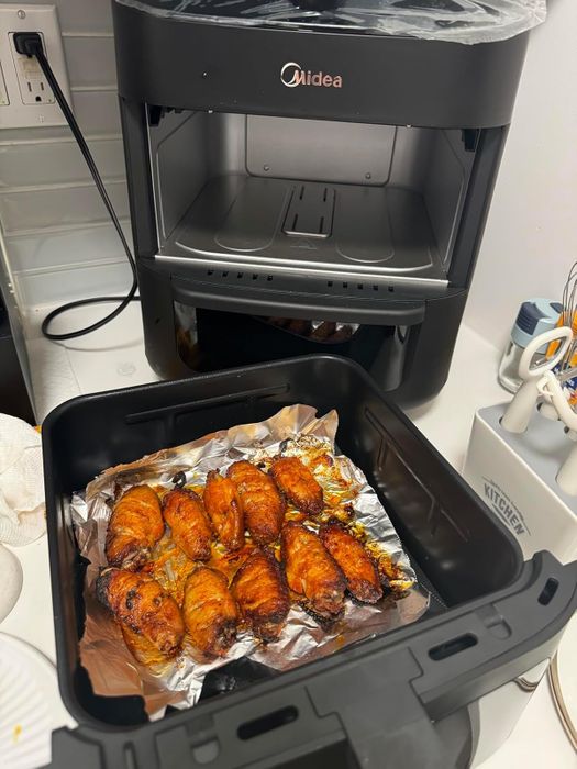 An air fryer with crispy, golden chicken wings on foil inside a kitchen setup