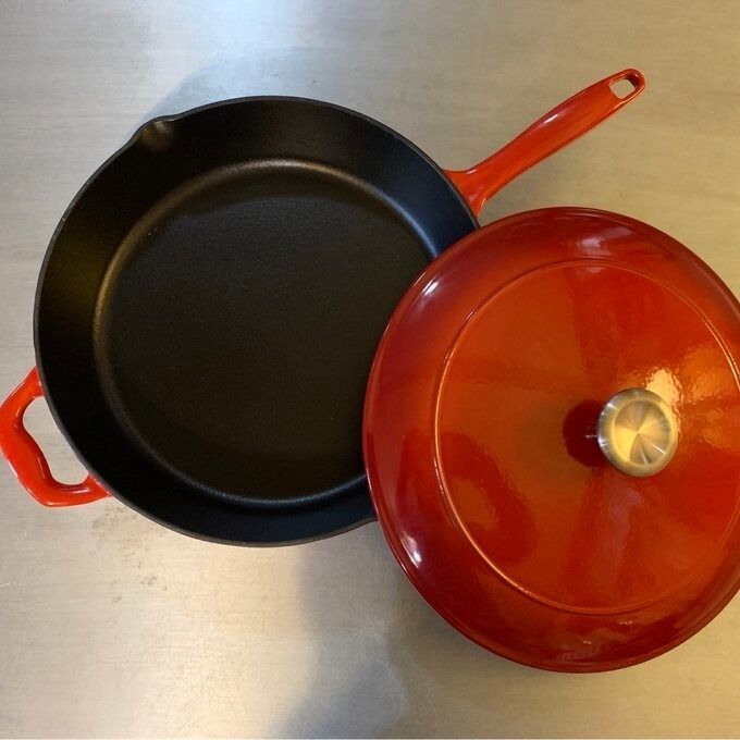 A cast-iron skillet and a red enameled cast-iron pot with a lid, elegantly placed on a kitchen countertop.