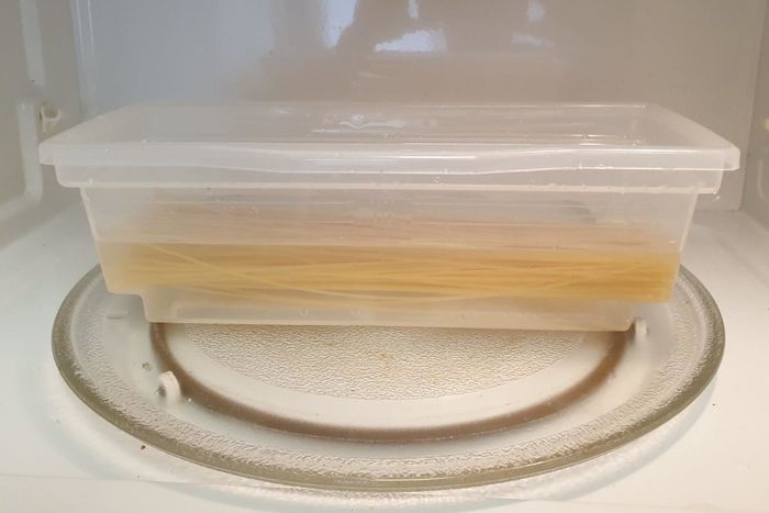 A reviewer’s photo showing uncooked pasta and water inside the clear, plastic microwave pasta cooker