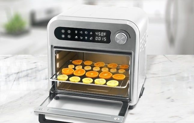 A countertop air fryer with fruit slices arranged on a rack