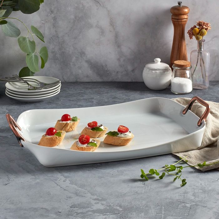 A white serving tray with copper handles