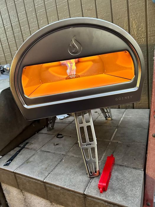 A portable pizza oven with a visible flame on a tiled surface, perfect for outdoor cooking