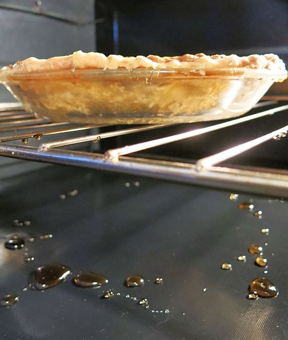 An oven liner catching drips from a pie baking inside the oven.