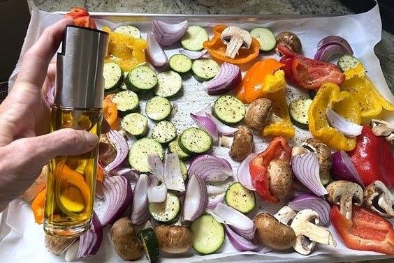 A reviewer spritzing vegetables with the oil mister