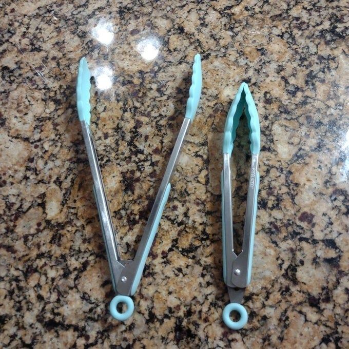 Two kitchen tongs with silicone handles resting on a granite counter