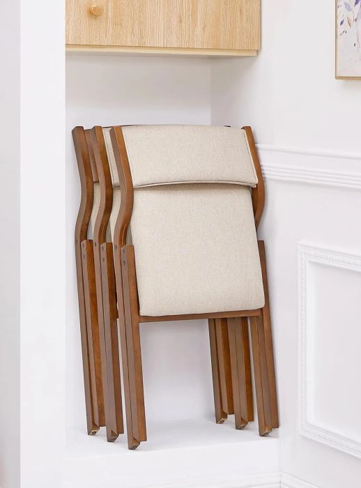 A beige folding chair with a wooden frame, resting against a white wall below a shelf