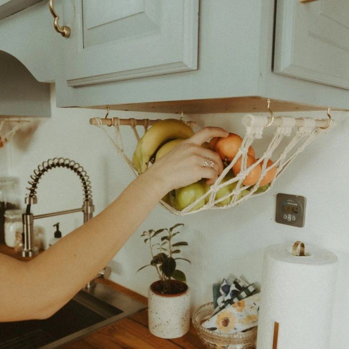 A hammock hanging from the bottom of a cabinet, holding several pieces of fruit.
