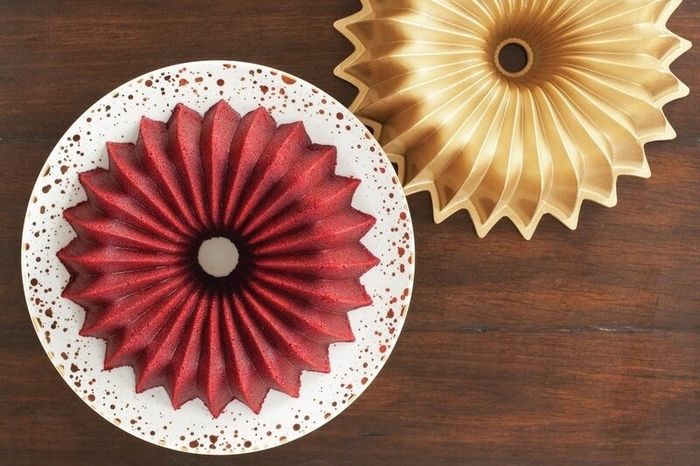 Two intricately designed Bundt cakes on a wooden table—one red, the other gold