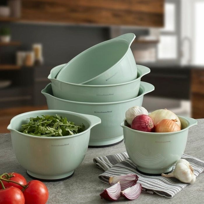 Four mixing bowls stacked on a kitchen counter with onions, arugula, and tomatoes in the background