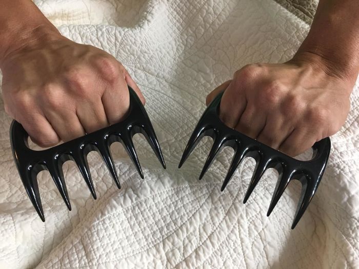A person gripping the handles of two claw-like shredders with their fingers